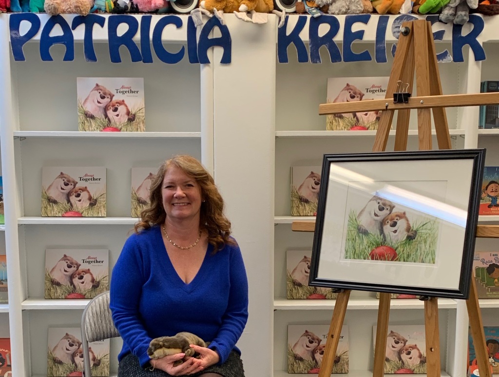 Author-illustrator Patricia Kreiser at her book launch at Children's Book World, with her picture book Better Together on the shelves behind her and an original illustration from the book on an easel.